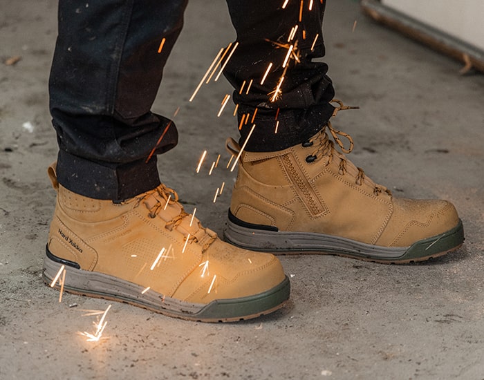 Close-up image of a person wearing a pair of Hard Yakka 3056 safety boots with welding sparks falling to the ground