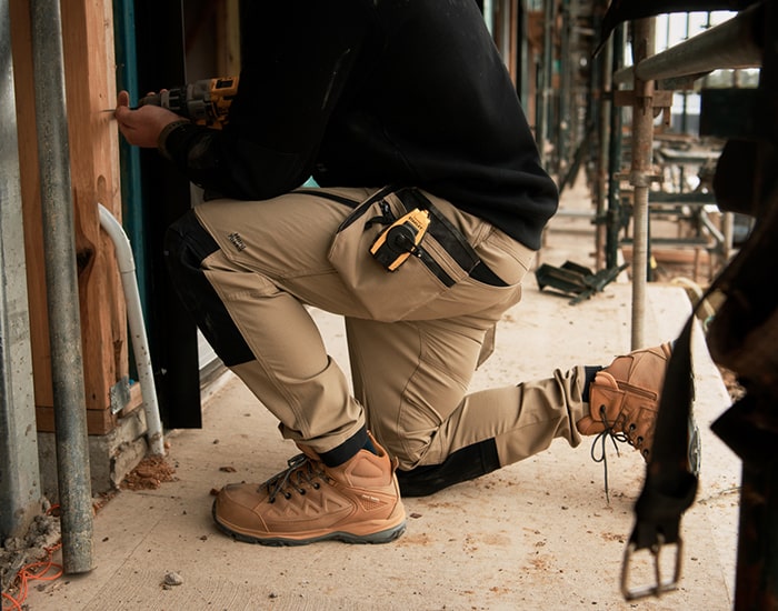 A man wearing Hard Yakka workwear drilling a hole in a wooden beam 