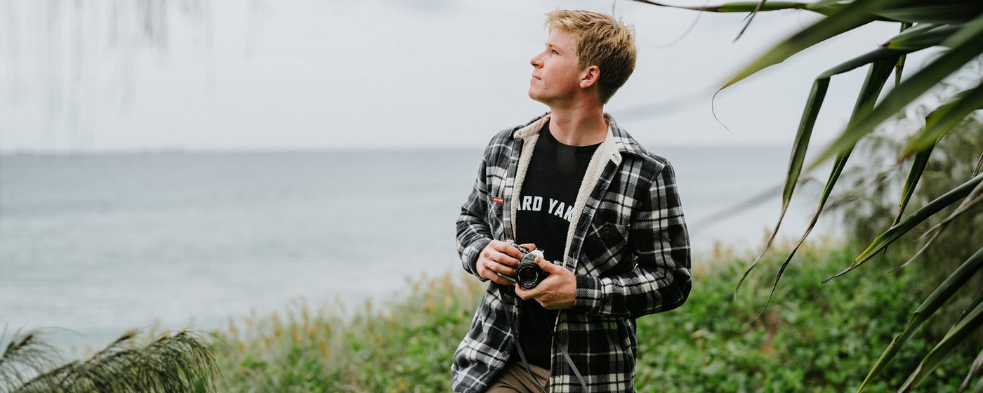 Hard Yakka brand ambassador, Robert Irwin wearing Hard Yakka clothing while holding a camera by the sea