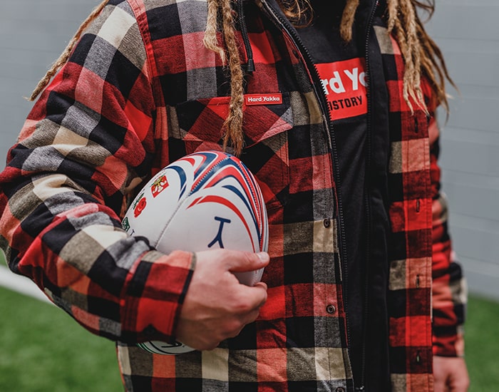 Close-up image of Jordy Reid holding a rugby ball, wearing Hard Yakka Quilted Shacket and T-Shirt