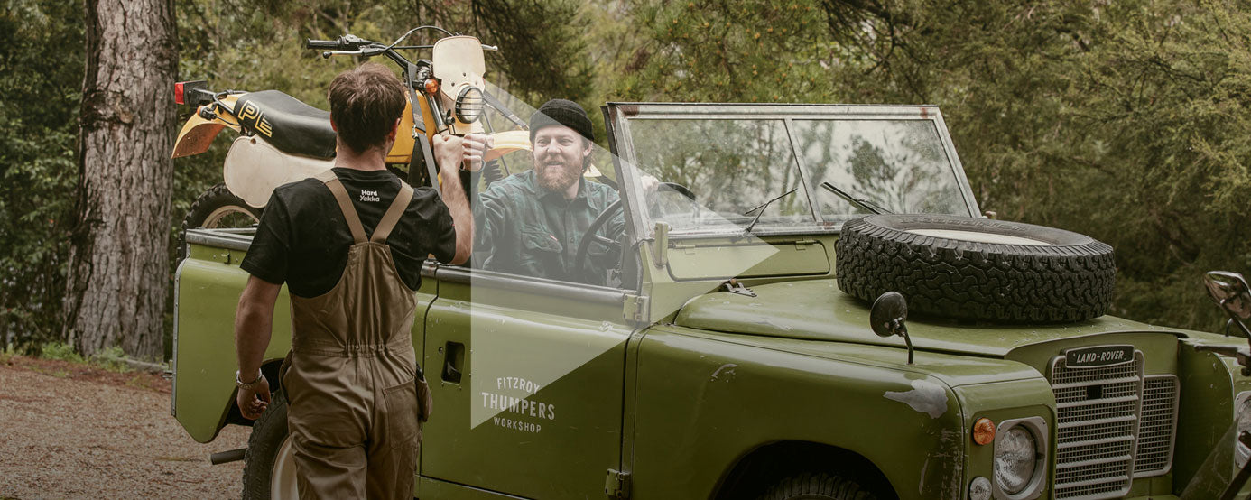 Elton King fist pumping with Brook James, who is driving a land rover with a motorcycle in the back. Both are wearing Hard Yakka workwear